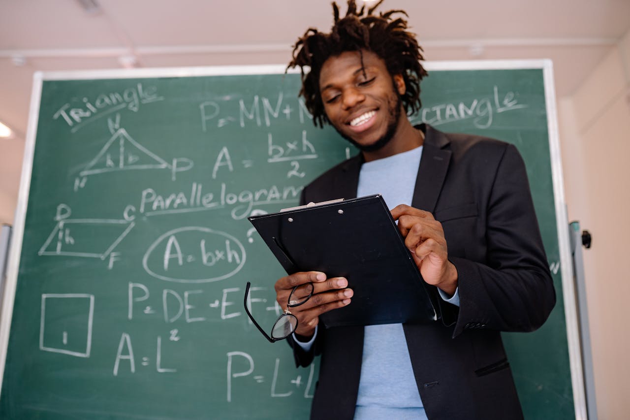A happy teacher standing in front of a blackboard with geometric formulas, holding a clipboard.